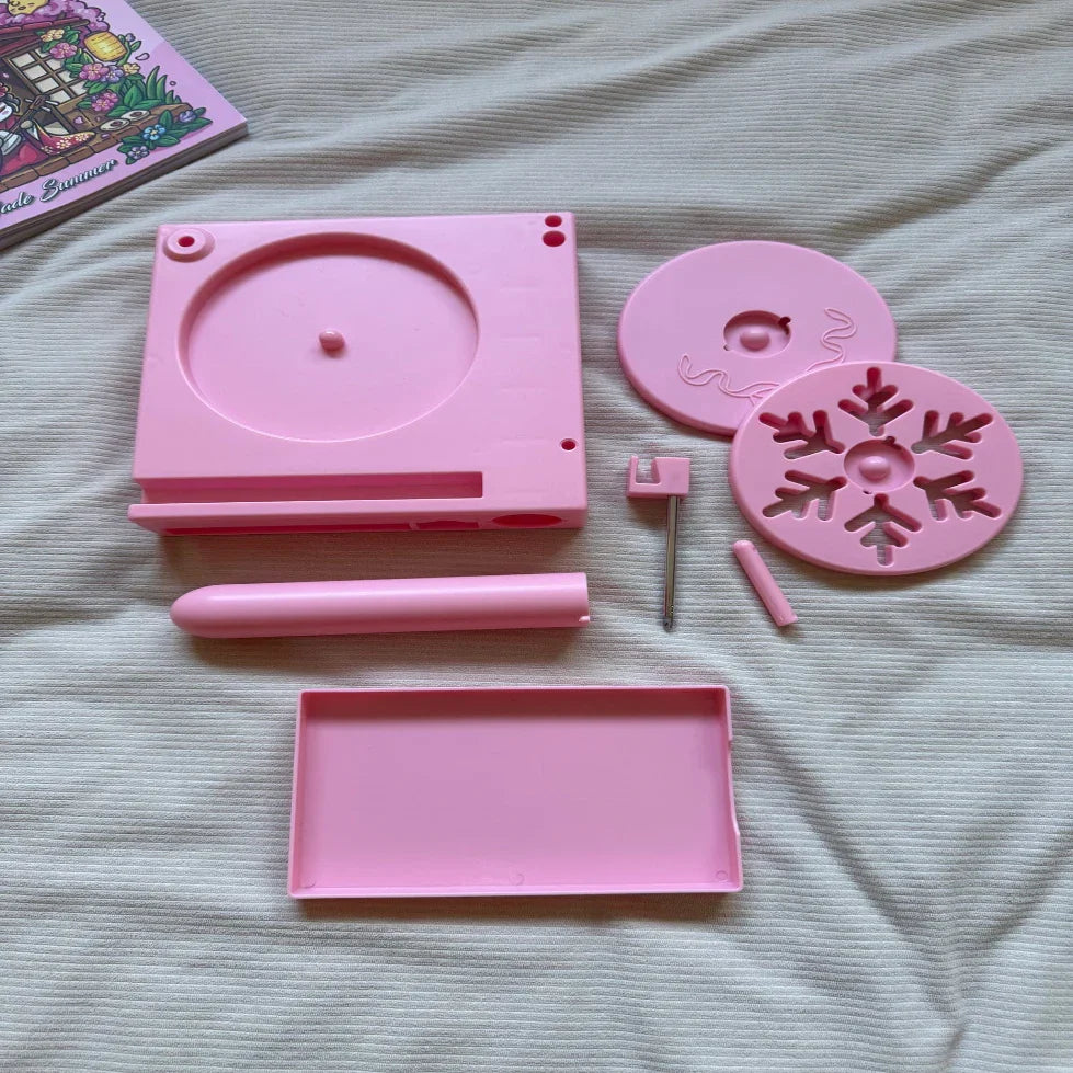 Pink plastic DIY arts and crafts kit parts laid out on a cream fabric surface