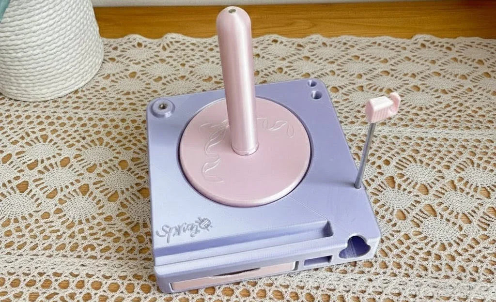 Pastel pink and purple yarn winder on lace tablecloth, crochet tool for yarn organization